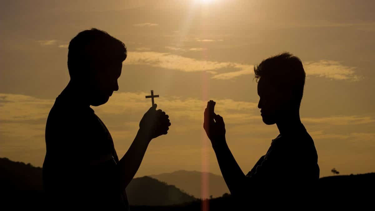 Two men silhouetted against a sunset sky, one holding a cross, symbolizing faith and spirituality.