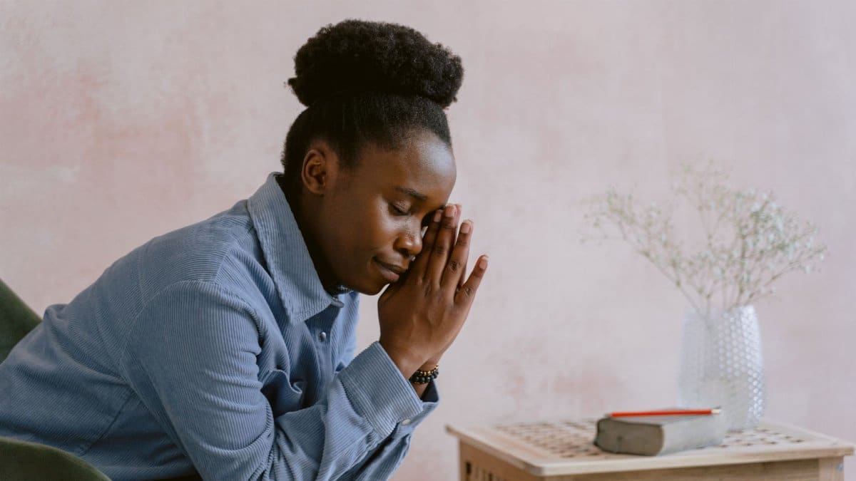 A peaceful woman indoors with eyes closed in prayer, conveying spirituality and devotion.