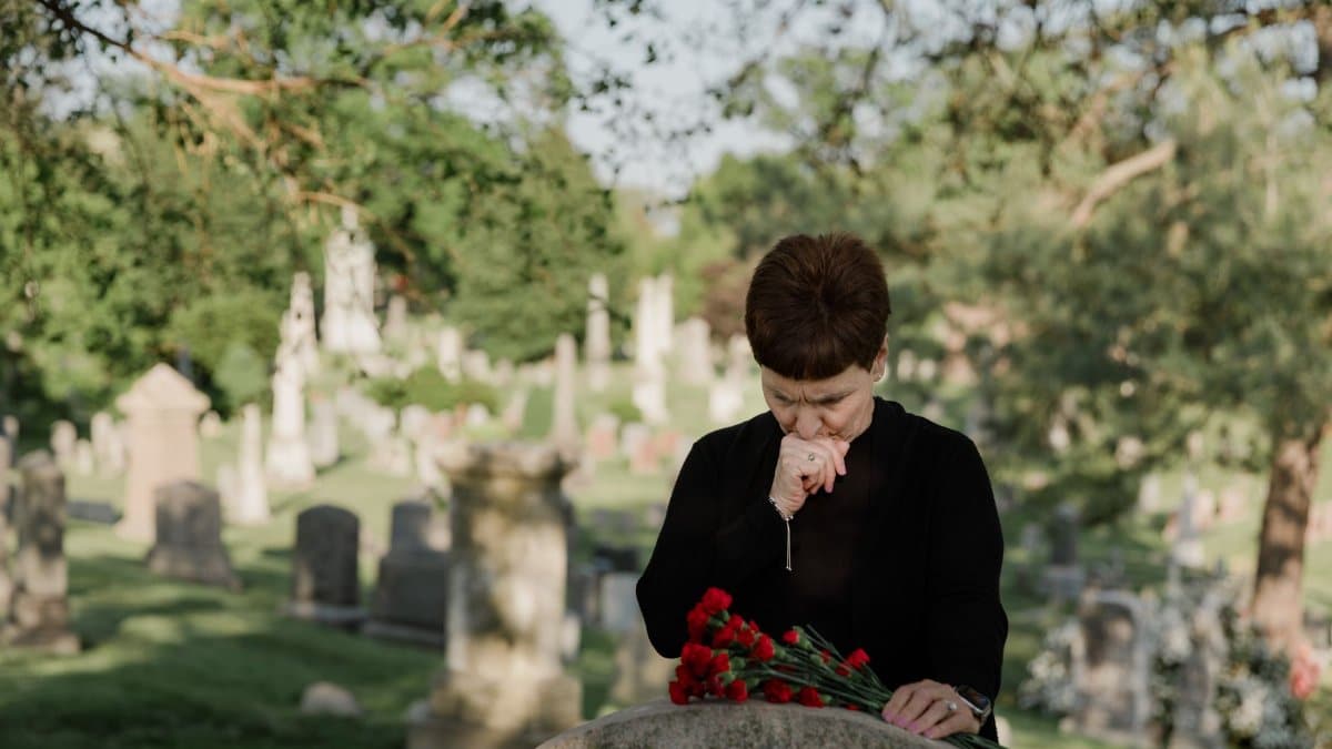 A woman in black paying her respects at a grave, holding flowers in a serene cemetery.