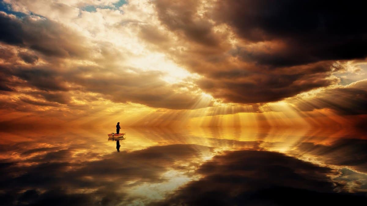 A lone boat floats on calm waters under a dramatic and vibrant sunset sky, casting reflections.