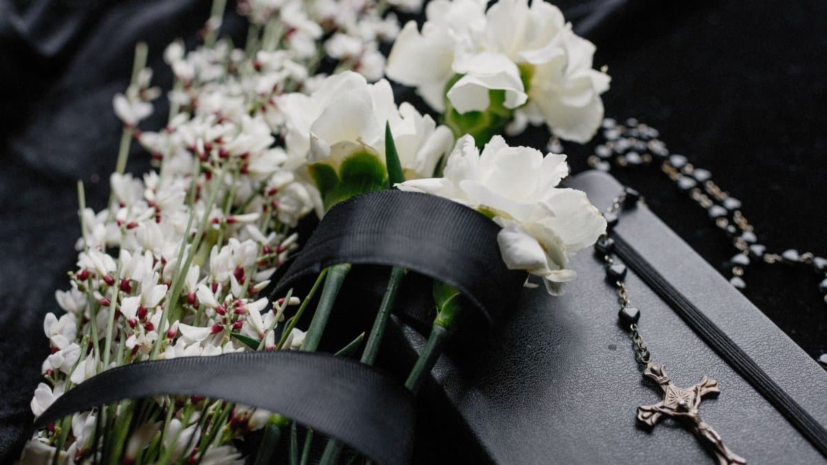 Close-up of white flowers and rosary on dark cloth, symbolizing mourning and spirituality.
