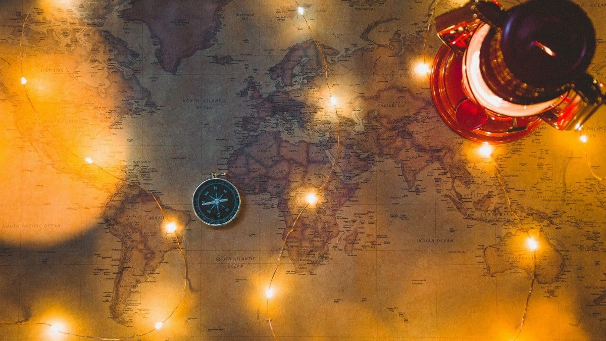 A vintage world map illuminated by string lights with a compass and lantern, evoking travel dreams.