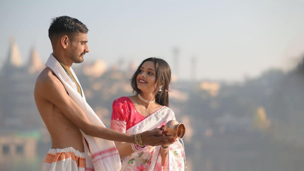 A joyful Indian couple in traditional attire performing a river ritual, embracing love and culture.