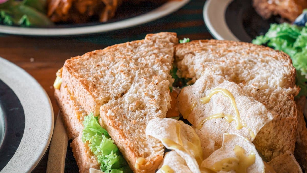 Close-up of a fresh sandwich with lettuce and chips on a wooden table, perfect for breakfast or lunch.