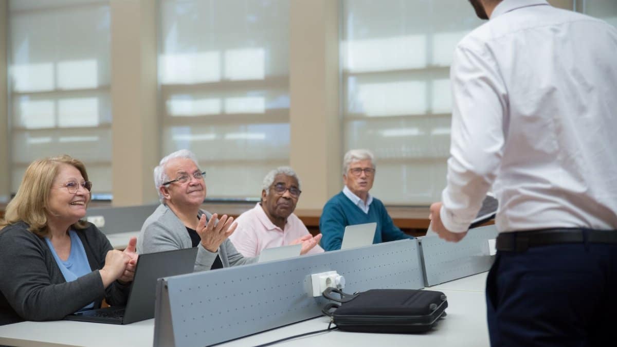 Senior adults attend a computer class, led by an instructor, in a classroom setting.