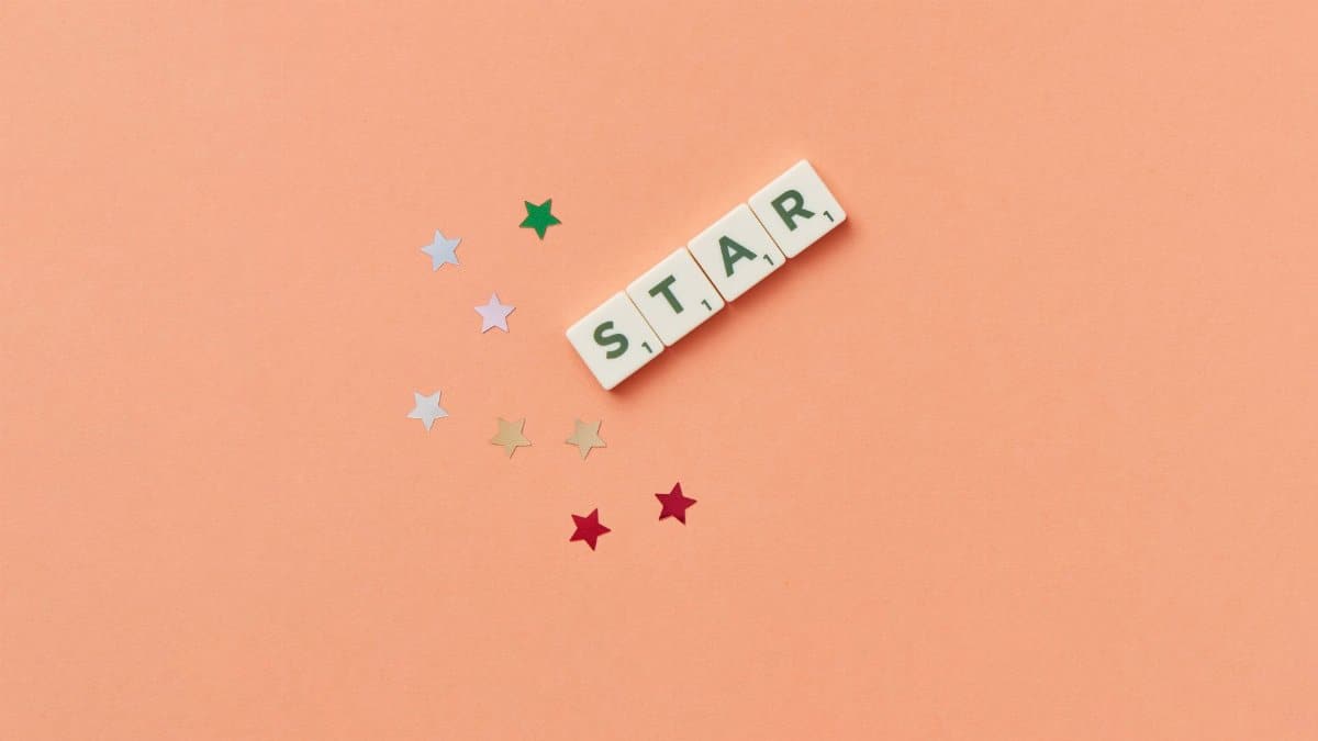 Flat lay image of Scrabble letters spelling 'STAR' on a peach background with colorful stars.