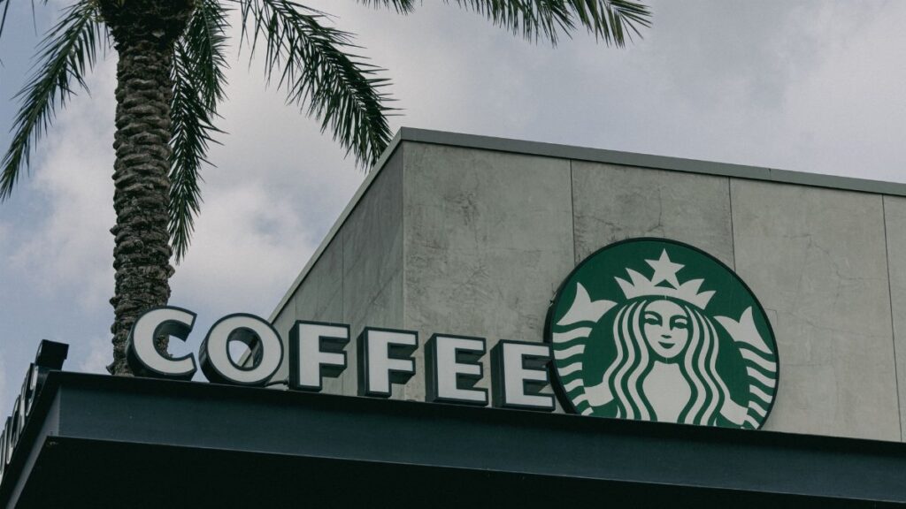 Low angle view of a Starbucks café sign with a palm tree against cloudy sky.