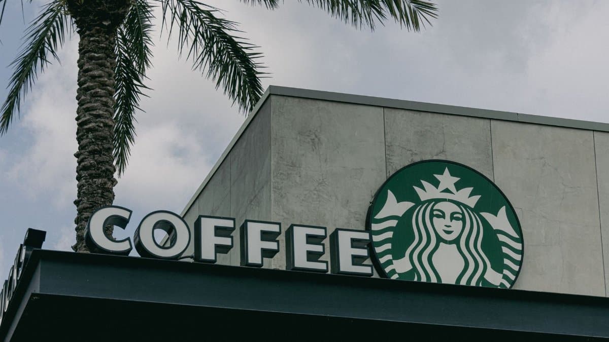 Low angle view of a Starbucks café sign with a palm tree against cloudy sky.