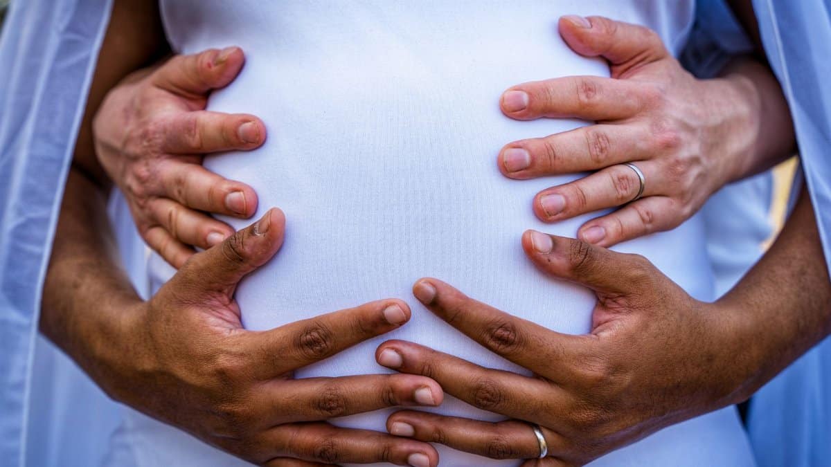 Close-up of diverse couple's hands lovingly embracing a pregnant belly symbolizing family and anticipation.