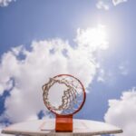 Low angle of basketball backboard with net hanging on hoop against clouds on blue sky