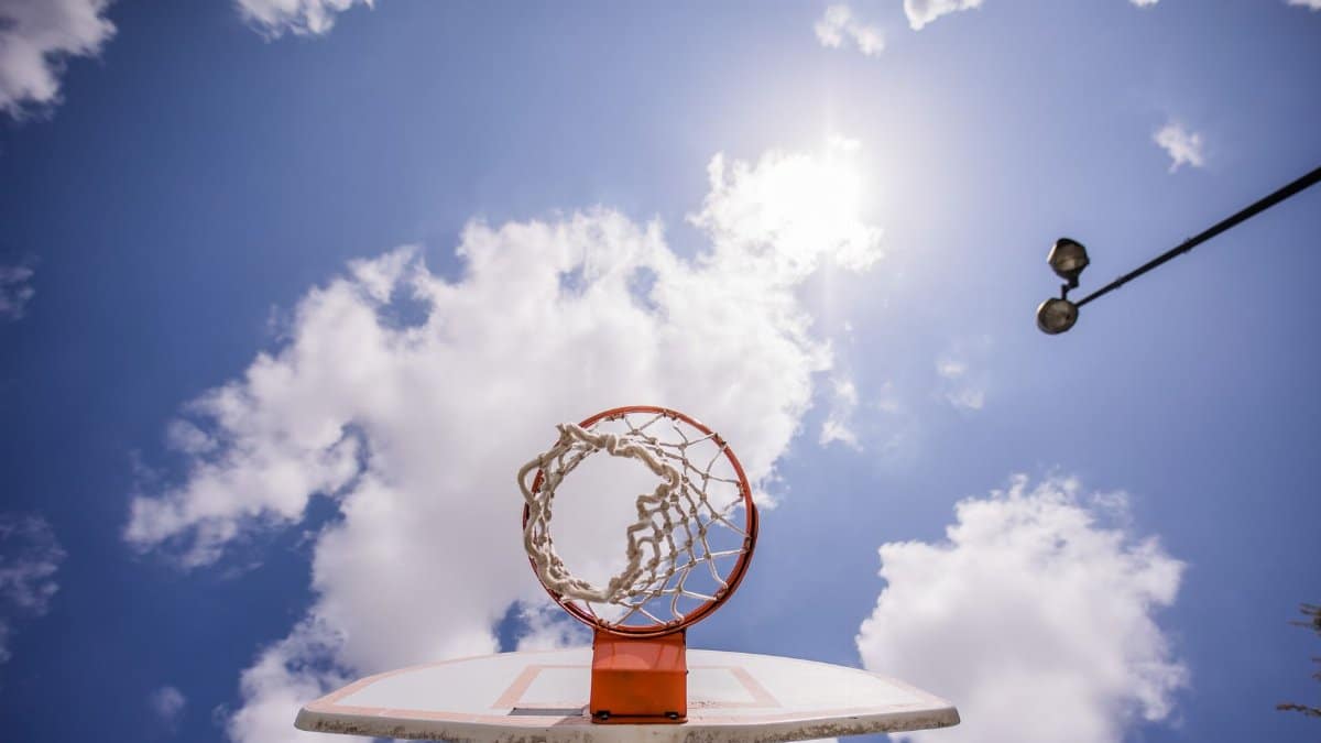 Low angle of basketball backboard with net hanging on hoop against clouds on blue sky