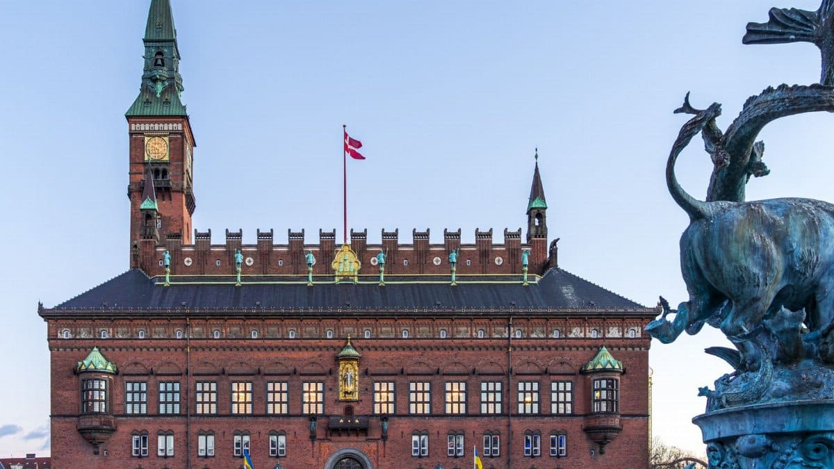 Twilight view of Copenhagen City Hall with the iconic Dragon Fountain and Danish flag.