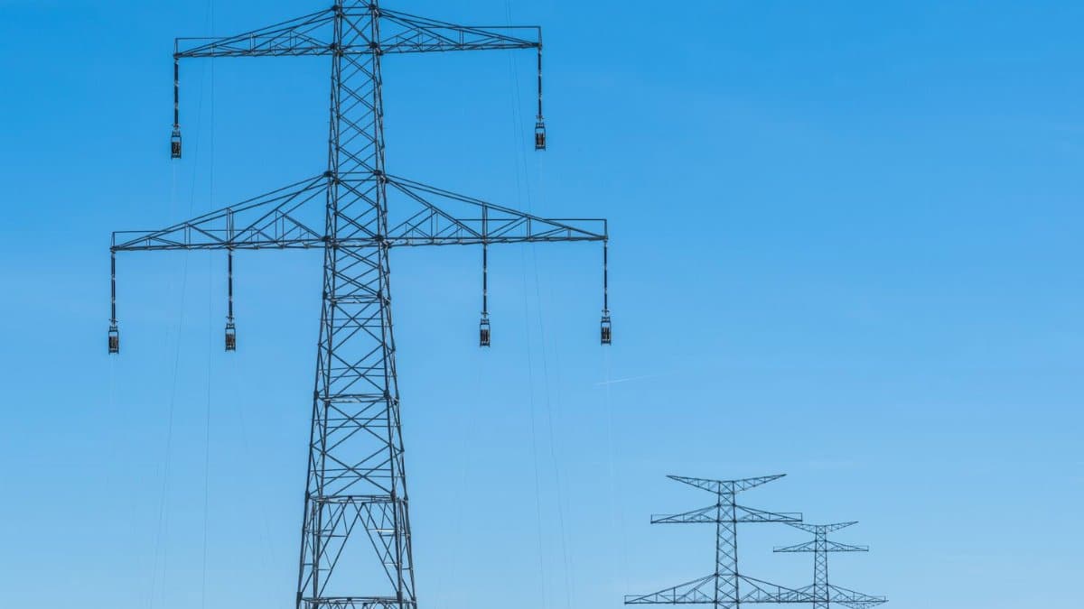 Blue sky over transmission towers on a rural landscape, symbolizing energy distribution.