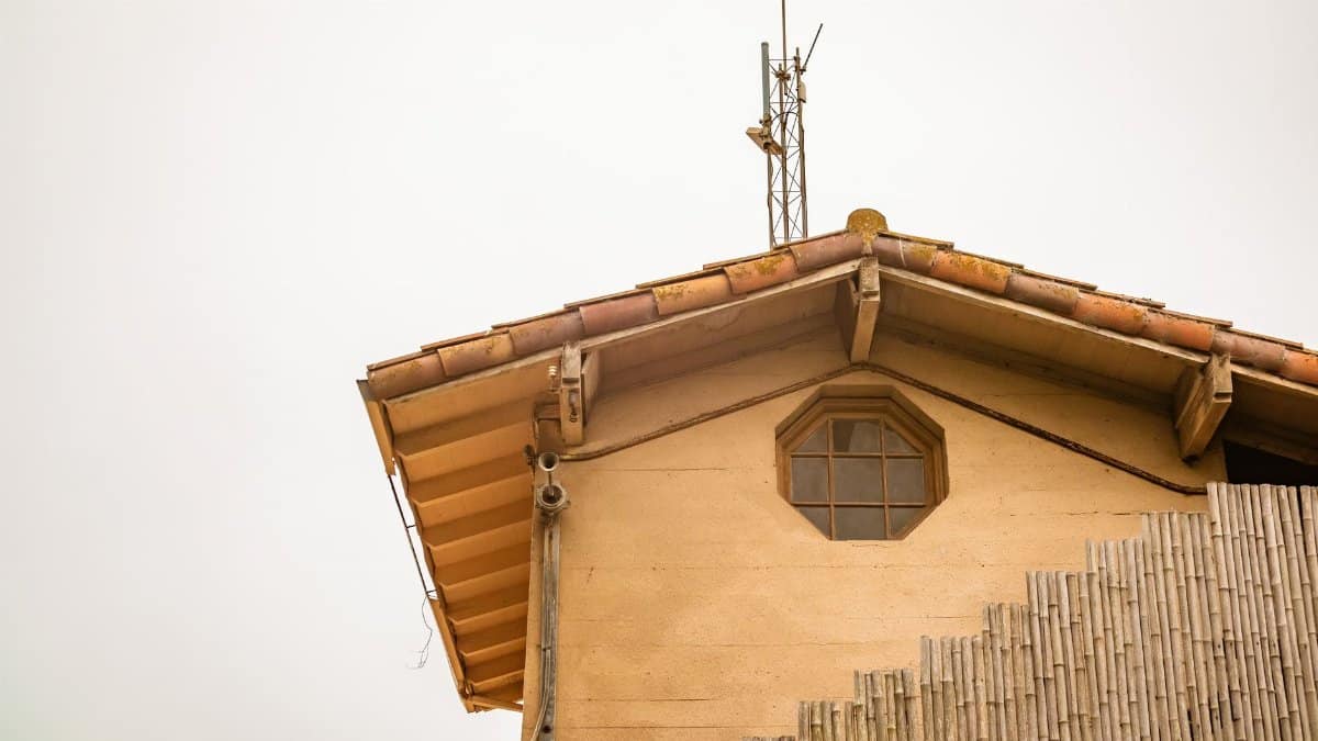 Low angle view of a rustic house roofline with antenna against clear sky, showcasing architectural details.