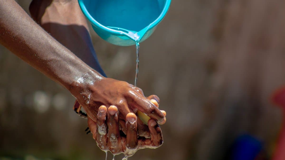 A close-up of hands being washed outdoors with flowing water and soap, promoting hygiene.