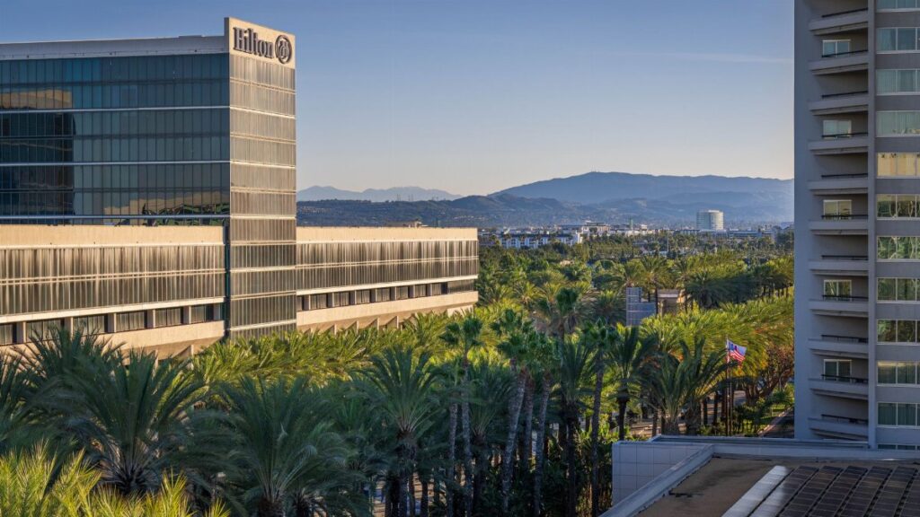 View of Hilton hotel surrounded by palm trees with mountains in the background at sunrise.