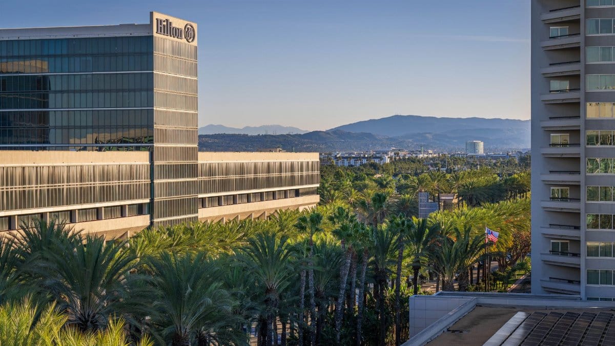 View of Hilton hotel surrounded by palm trees with mountains in the background at sunrise.
