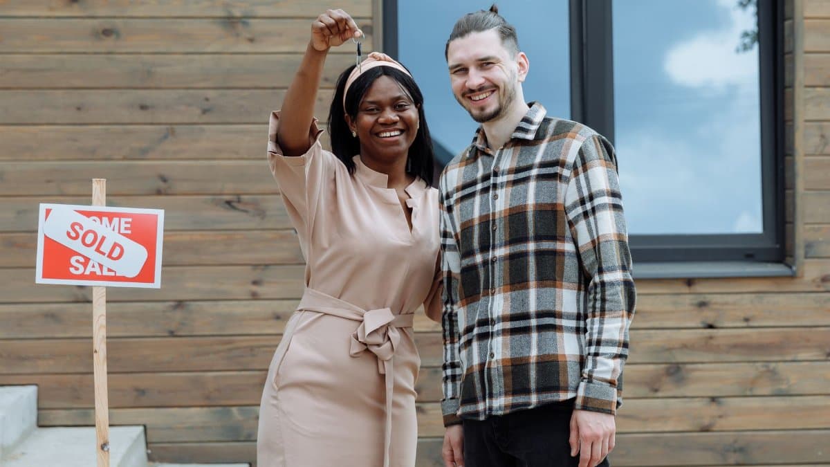 Young couple celebrates buying their first house with keys in hand and a sold sign.