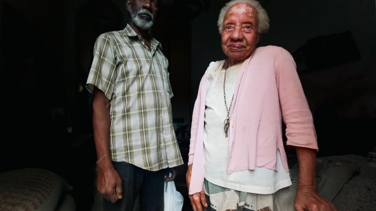 A portrait of an elderly couple standing together inside, expressing resilience.