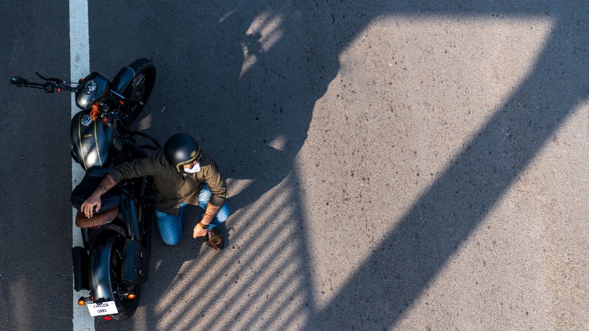 Aerial shot of a motorcyclist in a helmet resting beside his motorcycle on a sunny day.