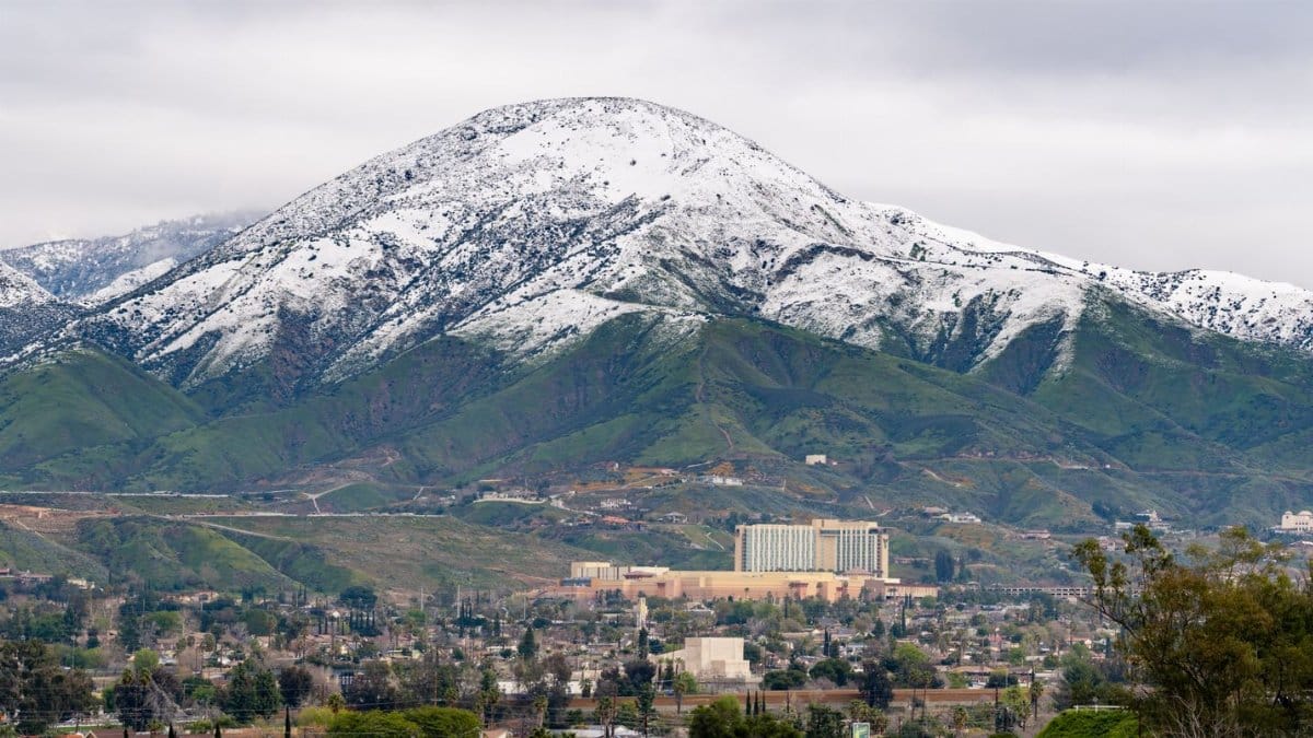 A winter aerial view of snow-capped mountains with San Bernardino cityscape in the foreground, California.