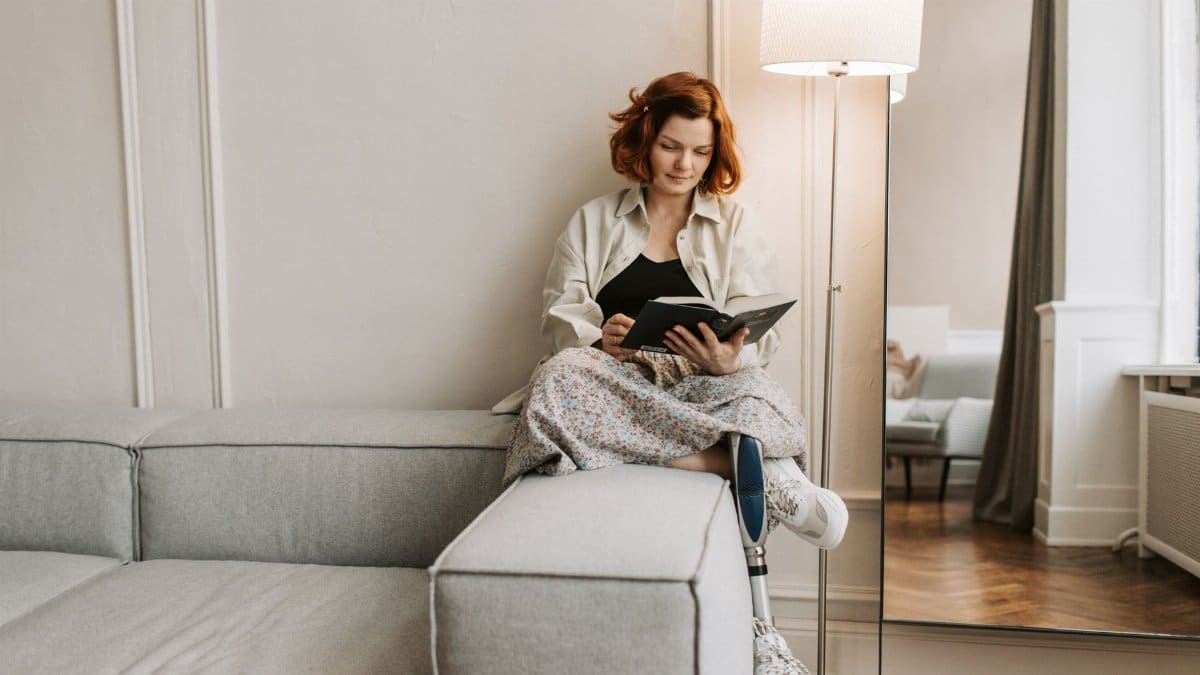 A woman with a prosthetic leg enjoys reading on a sofa in a cozy room.