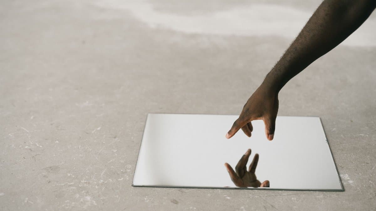 A hand reaching towards a reflective mirror surface creates an artistic visual impact.
