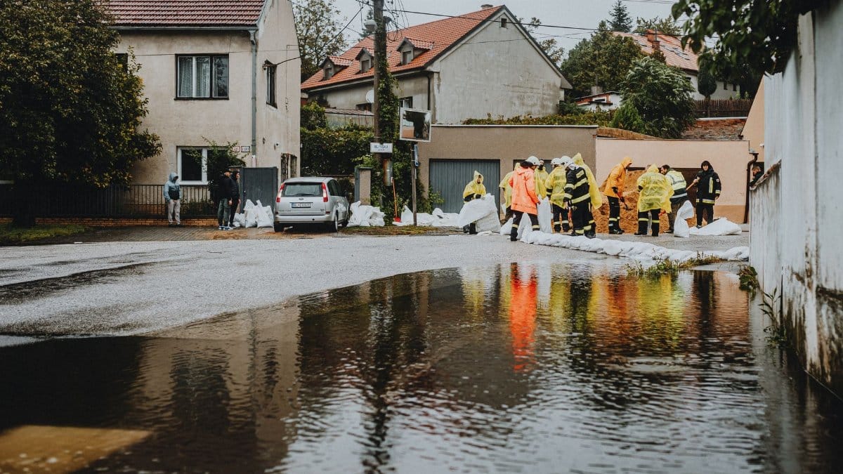 Emergency workers in rain gear manage floodwaters in a suburban street.