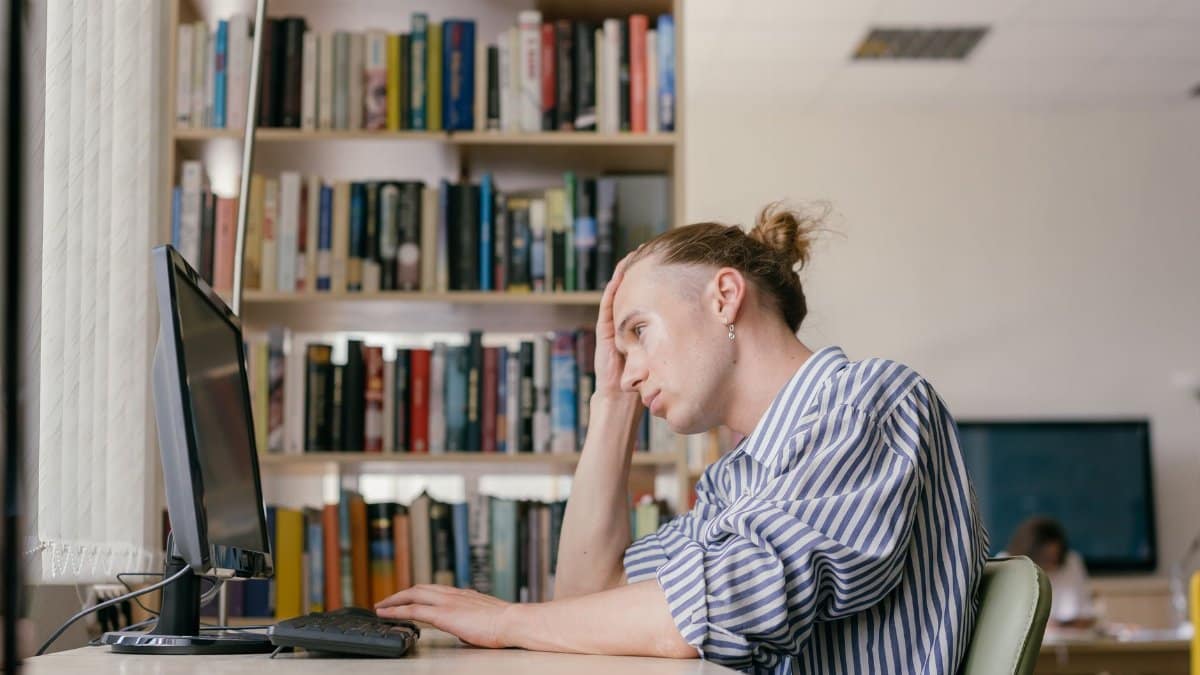 A young student working on a computer in a library setting, deep in thought.