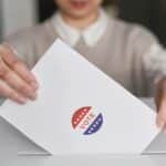 A person casting a vote by placing a ballot into a ballot box, symbolizing democratic participation.