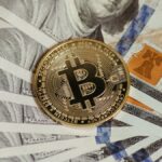 A Bitcoin coin placed on a stack of hundred dollar bills, symbolizing cryptocurrency and traditional wealth.