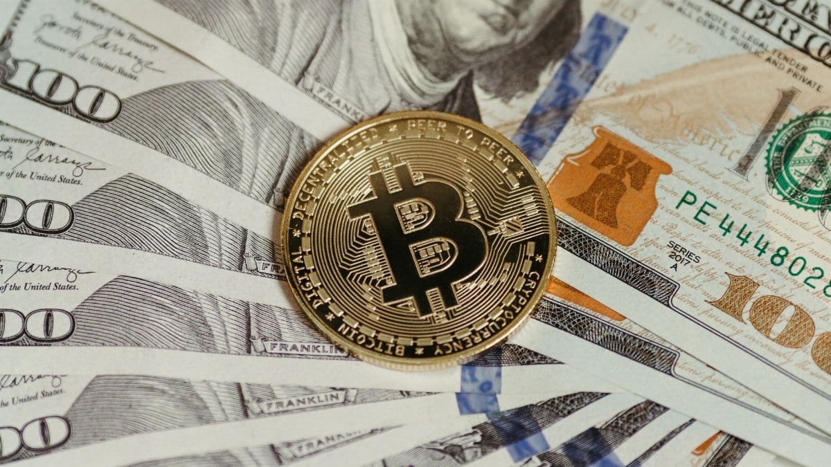 A Bitcoin coin placed on a stack of hundred dollar bills, symbolizing cryptocurrency and traditional wealth.