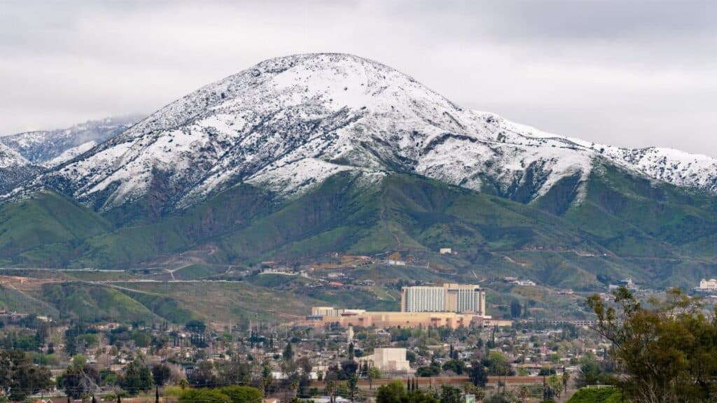 A winter aerial view of snow-capped mountains with San Bernardino cityscape in the foreground, California.