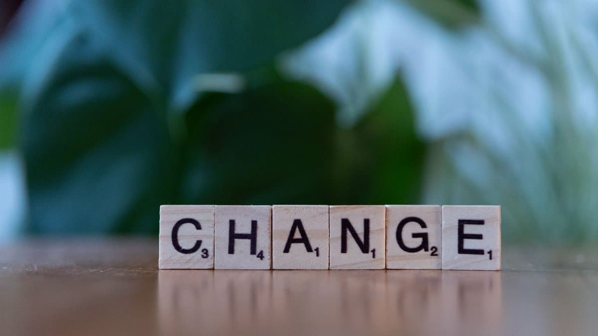 Scrabble tiles spelling 'CHANGE' on a wooden surface with a blurred green background.