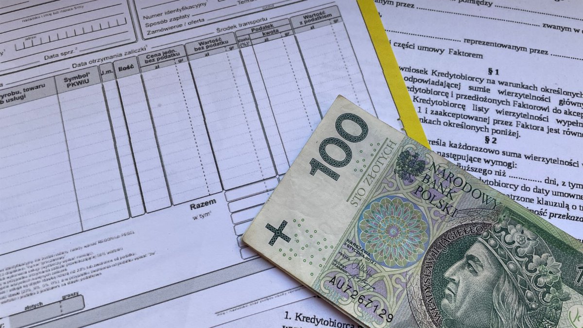 100 Polish zloty bill on top of financial documents and invoices on desk.