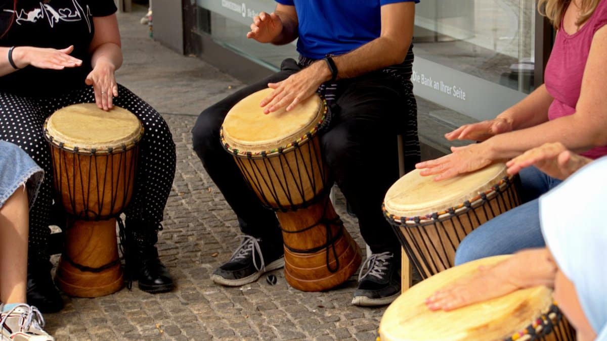 Adults playing African djembes outdoors, creating rhythm and music in a public space.
