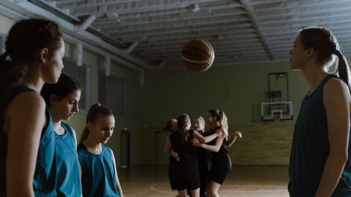 Young female basketball players in a dimly lit indoor court showing emotions.