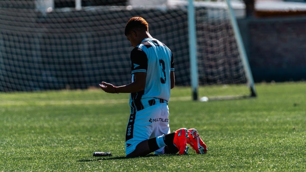 A soccer player kneels on the field, reflecting after a game, in a contemplative pose.
