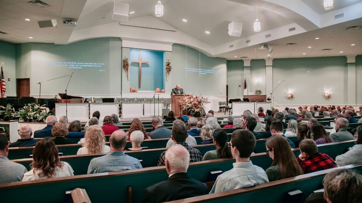 A large congregation listens to a speaker in a modern church setting.