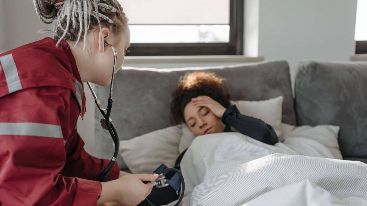 A paramedic examines a sick woman with a stethoscope indoors, providing medical care.