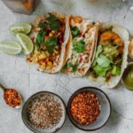 Top view of colorful Mexican tacos with limes, spices, and sauces, perfect for a culinary splash.
