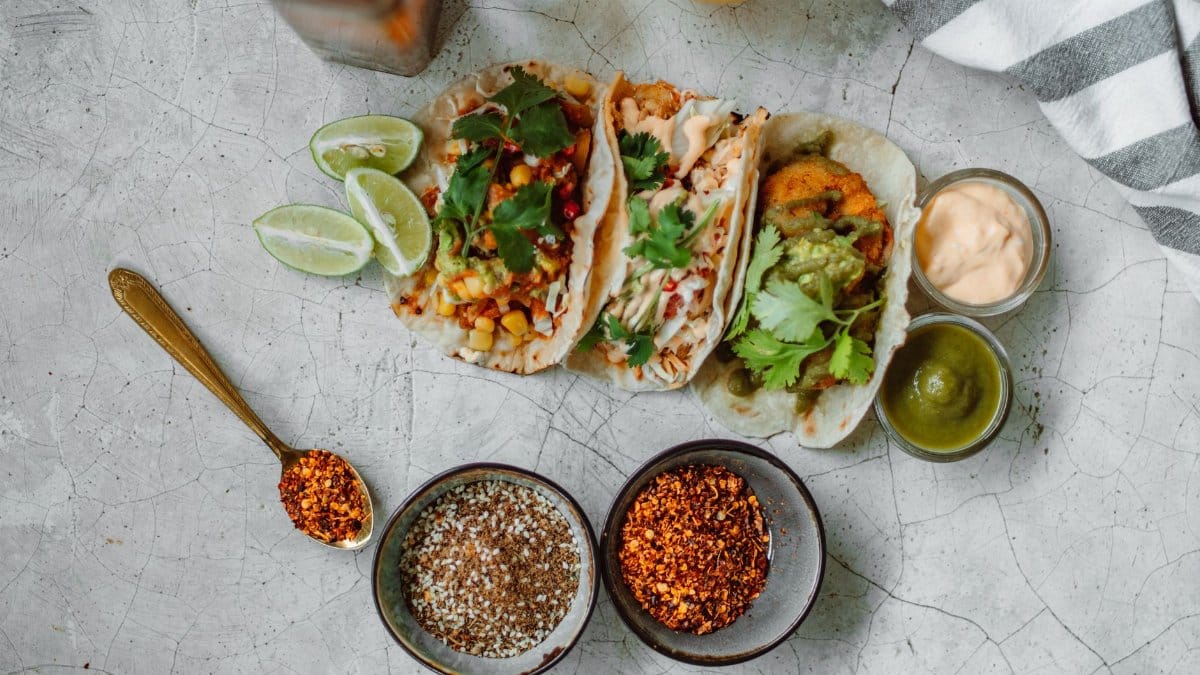 Top view of colorful Mexican tacos with limes, spices, and sauces, perfect for a culinary splash.