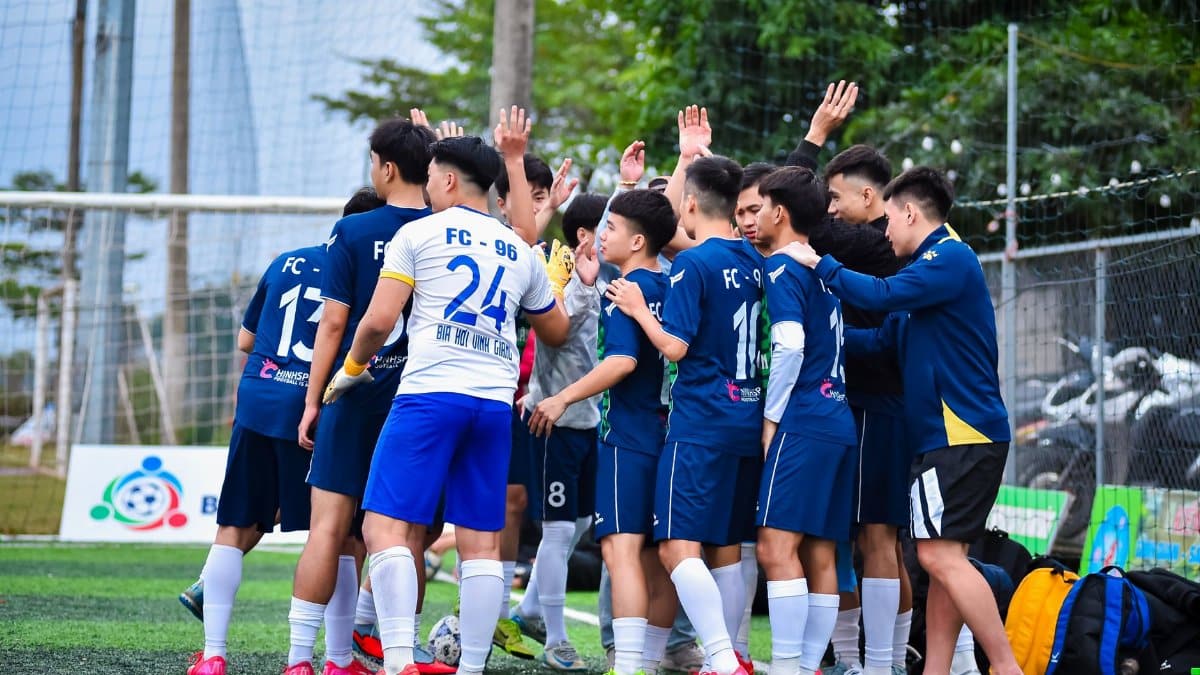 A soccer team in a group huddle on a grassy football field in Hanoi, Vietnam.