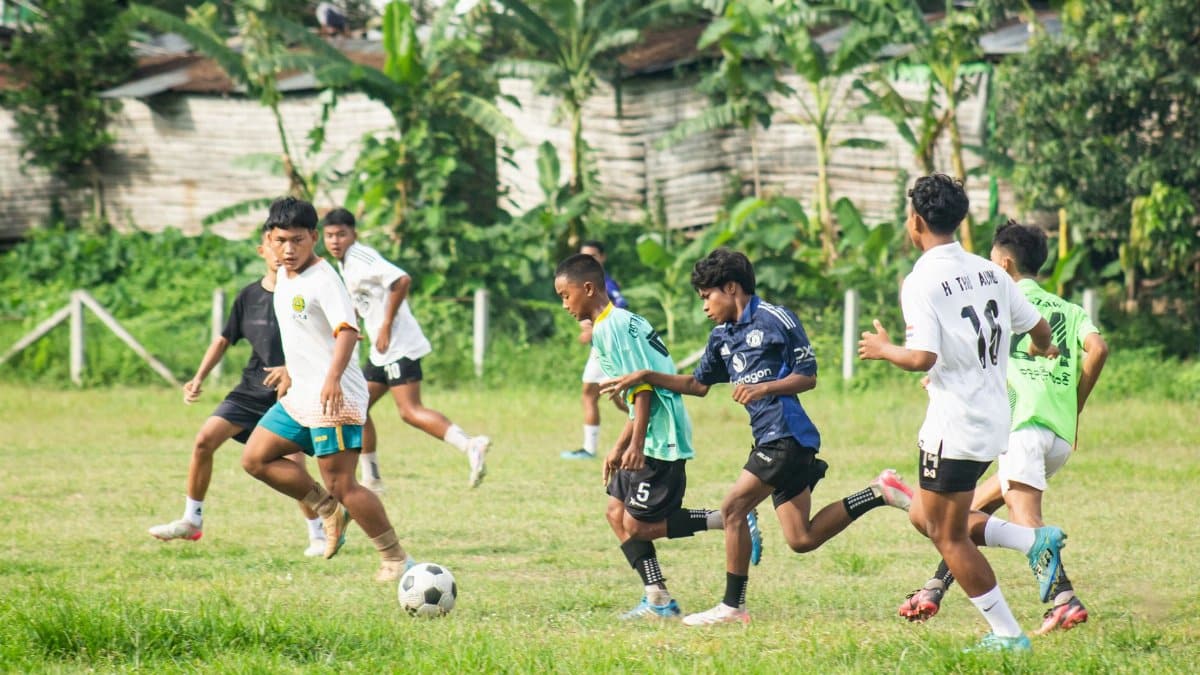 Young boys playing an intense soccer match on a grassy field in Myawaddy, Myanmar.