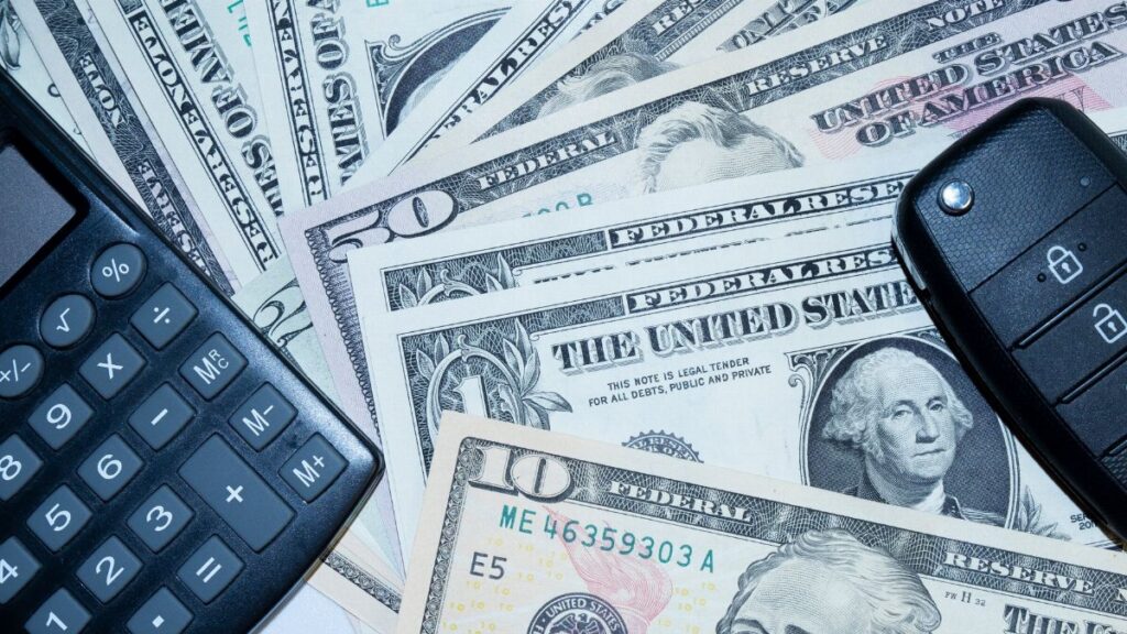 US dollars, calculator, and car keys representing finance and investment tools.