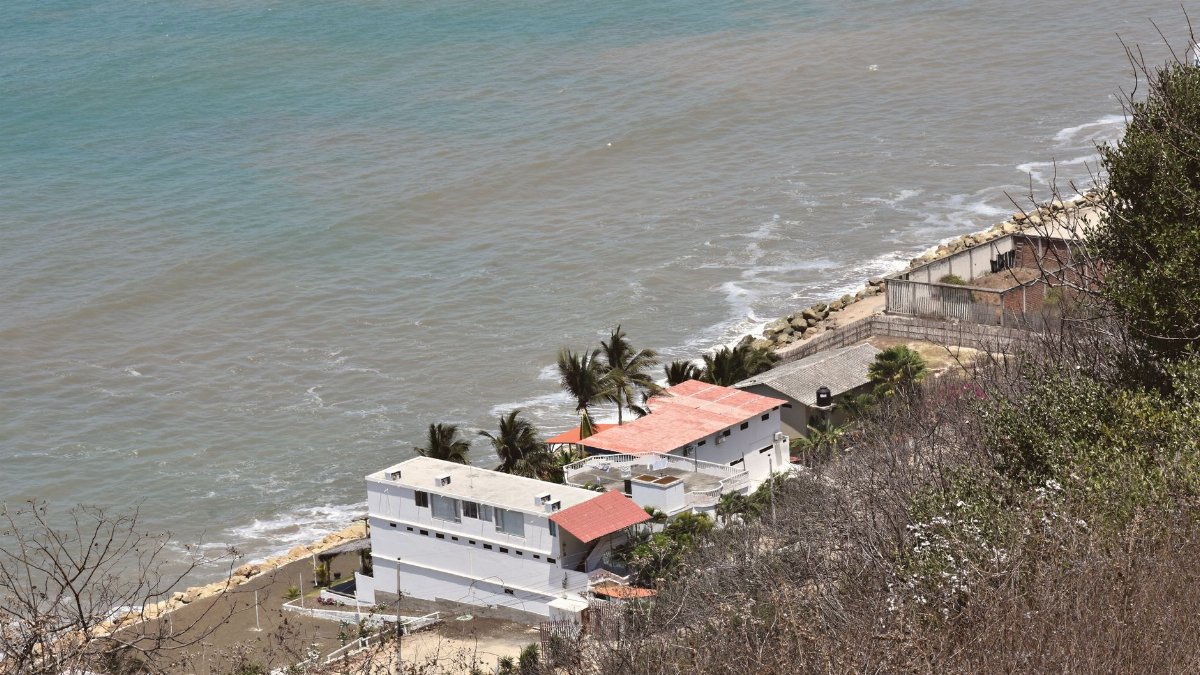 Aerial view of coastal homes along the shoreline in Ecuador, featuring clear ocean waters and lush greenery.