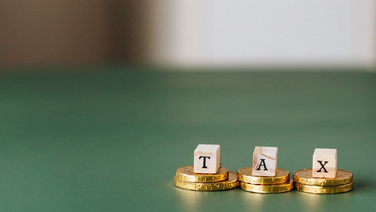 Stacked gold coins with wooden blocks spelling 'TAX' on a green backdrop.