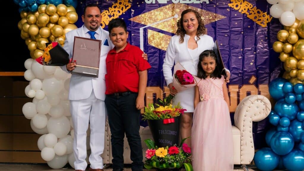 Family celebrating a graduation with flowers and balloons indoors.