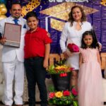 Family celebrating a graduation with flowers and balloons indoors.