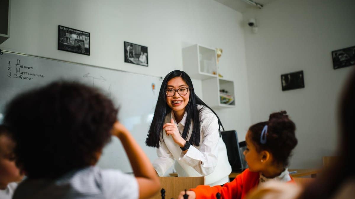 A teacher interacts with children during a chess lesson in a classroom setting.
